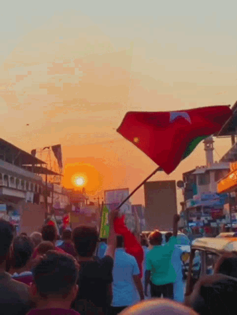 a crowd of people holding flags in front of a sunset with a sign that says ' tesco ' on it