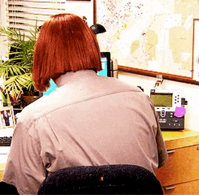 a woman with red hair is sitting at a desk with a phone and a map on the wall behind her