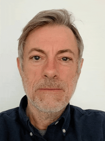 a man with a beard wearing a blue shirt looks at the camera