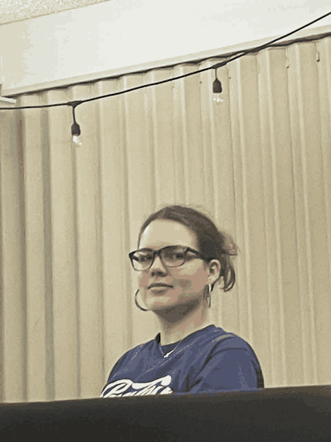 a woman wearing glasses and a blue shirt that says coca cola on it