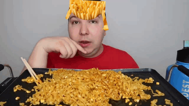 a man in a red shirt is eating noodles with french fries on his head