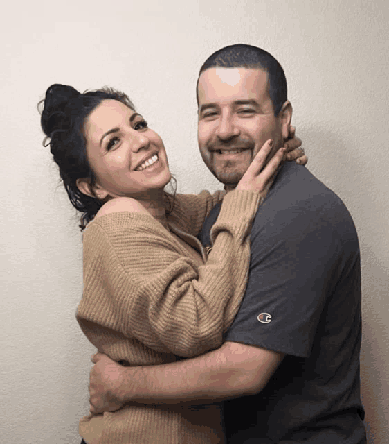 a man wearing a champion shirt is hugging a woman in a tan sweater