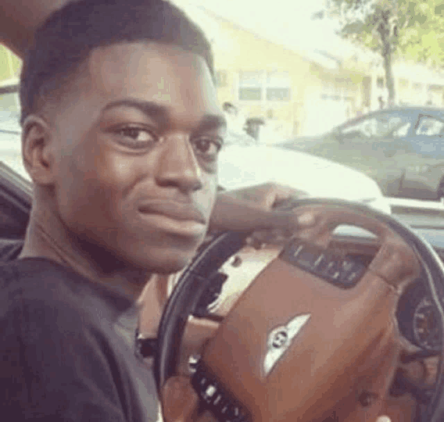 a young man is sitting in the driver 's seat of a bentley .