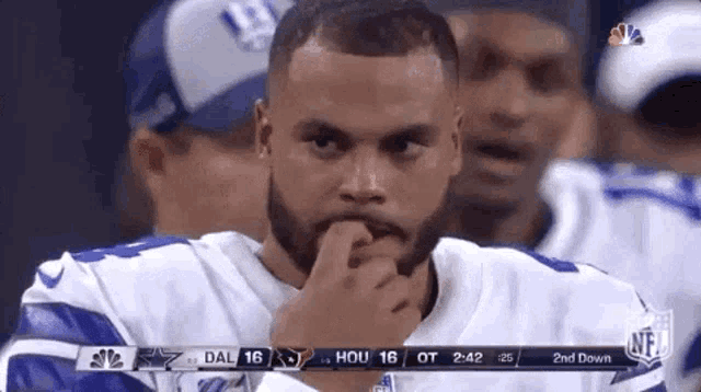 a man with a beard is sitting on the sidelines of a football game with his hand on his chin .