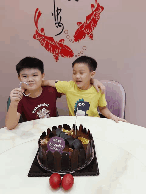 two boys are sitting at a table with a cake that says happy birthday carsel