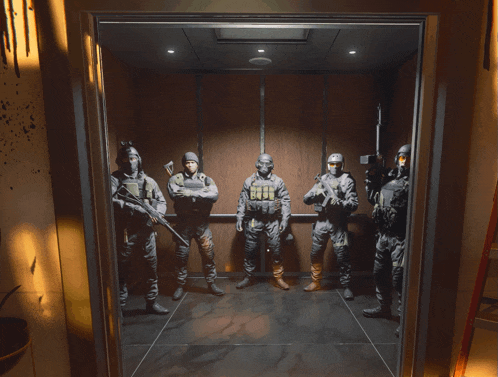 a group of soldiers are standing in an elevator and one of them is wearing a helmet with the letter g on it