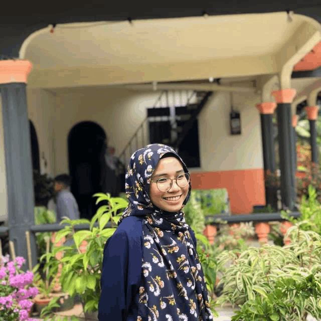 a woman wearing a hijab and glasses is smiling in front of a house