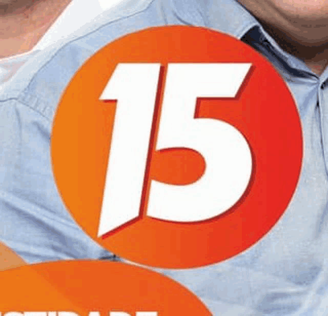 a man in a blue shirt is standing in front of a red circle with the number 15 on it