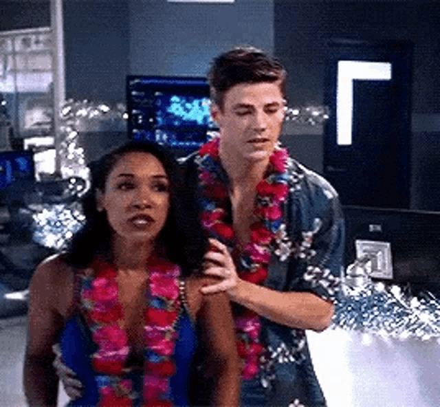 a man and a woman are standing next to each other in a room wearing lei .