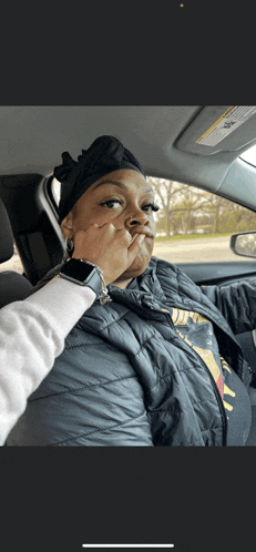 a woman sitting in a car making a face with her hand