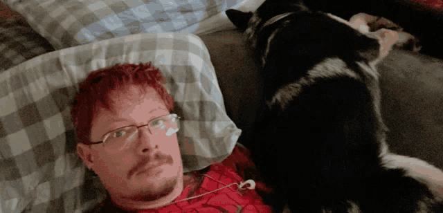 a man with red hair and glasses is laying on a bed with his dog