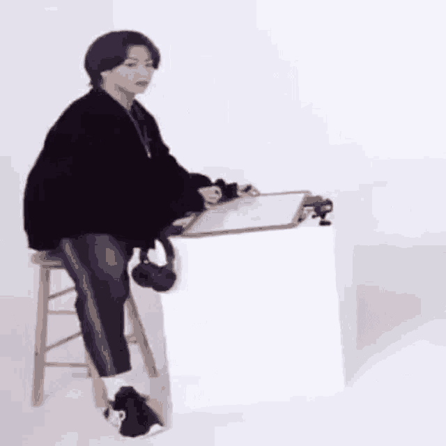 a person is sitting on a stool in front of a desk with a clipboard .