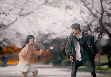 a man and a woman are standing next to each other in a park with cherry blossom trees in the background .