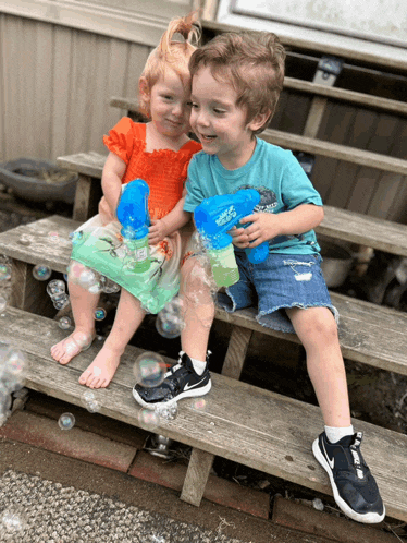 a boy and a girl are playing with soap bubble guns