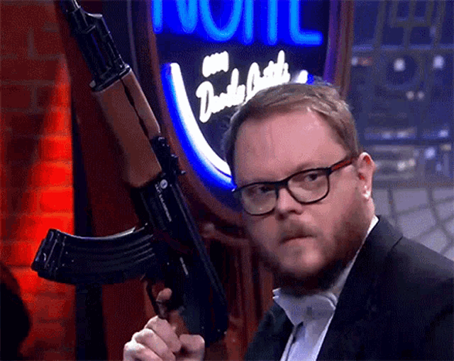 a man in a suit and glasses holds a gun in front of a neon sign that says dusty smith