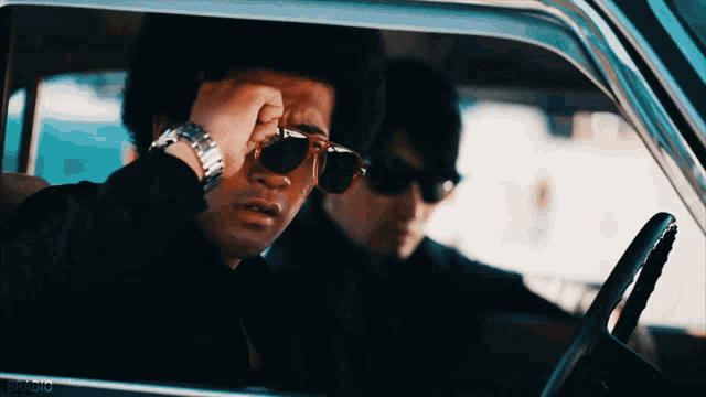 a man wearing sunglasses and a watch is sitting in a car next to another man wearing sunglasses