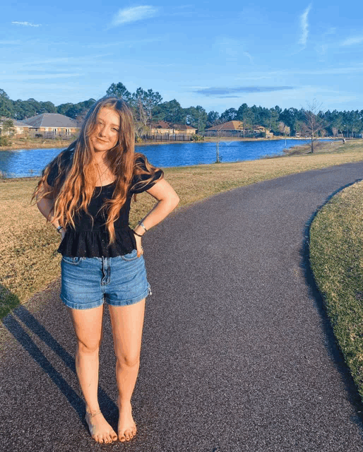 a woman in shorts and a black top is standing on a path near a lake