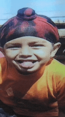 a young boy wearing a turban and an orange shirt is sticking his tongue out .