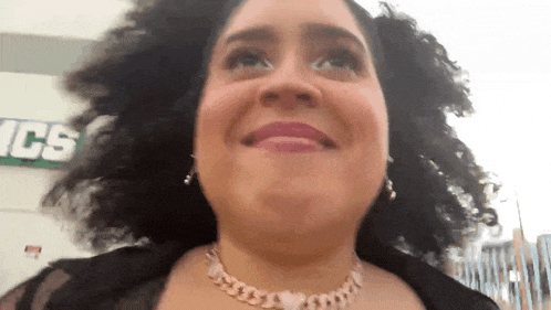 a woman with curly hair and a necklace is smiling in front of a sign that says ics