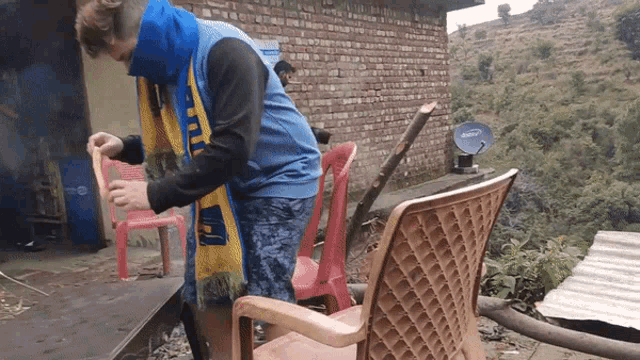 a man wearing a blue and yellow scarf is standing next to a chair with a satellite dish on it