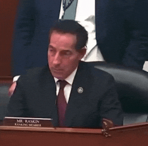 a man in a suit and tie is sitting at a desk with a name tag that says mr. raskin