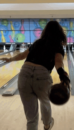 a woman is throwing a bowling ball in a bowling alley with a scoreboard behind her that says paradise bowl