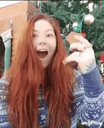 a woman with red hair is standing in front of a christmas tree holding a card in her hand .