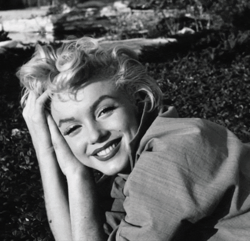 a black and white photo of a smiling woman laying in the grass