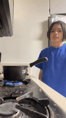 a young boy in a blue shirt is cooking on a stove top