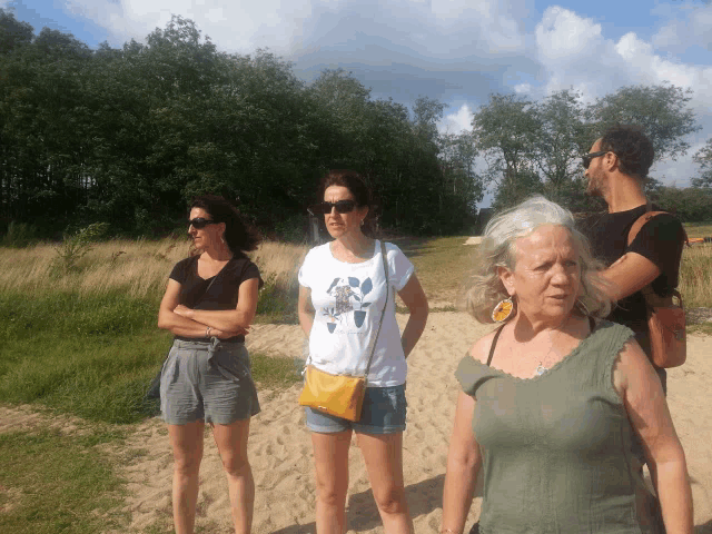 a group of people standing on a sandy beach with one woman wearing a white shirt with a turtle on it