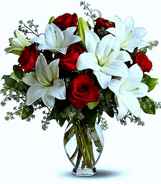 a vase filled with red roses , white lilies and greenery .