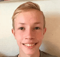 a young man is smiling for the camera and wearing a grey shirt .