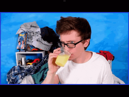 a man drinking from a cup in front of a pile of clothes and a box that says america on it