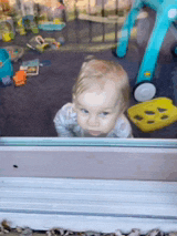 a baby is looking out of a window at toys on the floor