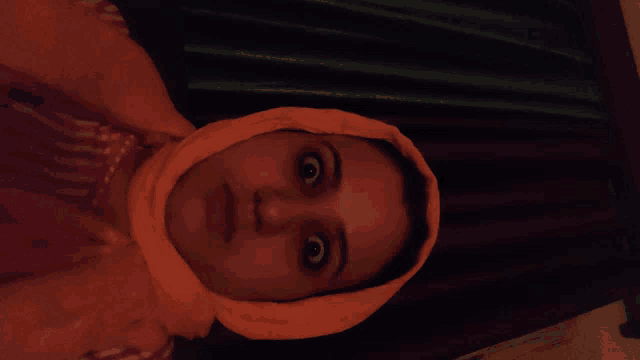 a woman with an orange scarf around her head looks at the camera