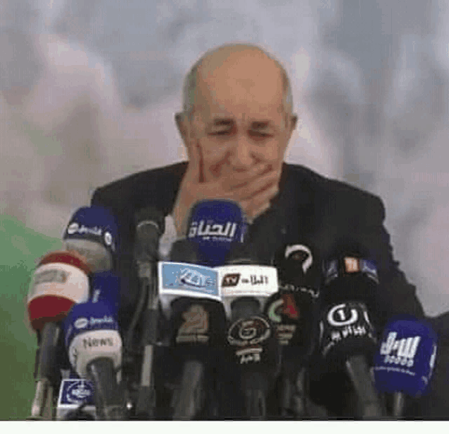 a man is covering his mouth with his hand while sitting in front of a bunch of microphones .