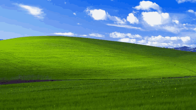 a grassy hill with a blue sky and white clouds in the background