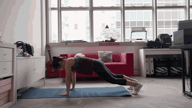 a woman is doing push ups on a blue mat in front of a red couch and a sign that says build yours