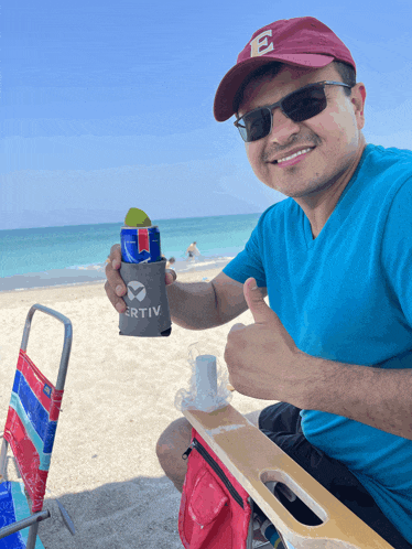 a man wearing a red hat with the letter e on it is sitting on the beach