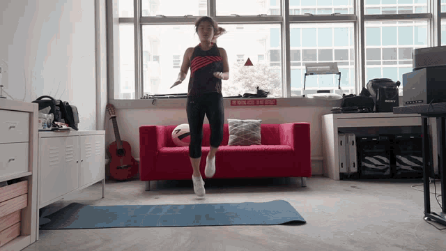 a woman is jumping in front of a red couch in a room with a sign on the wall that says no smoking