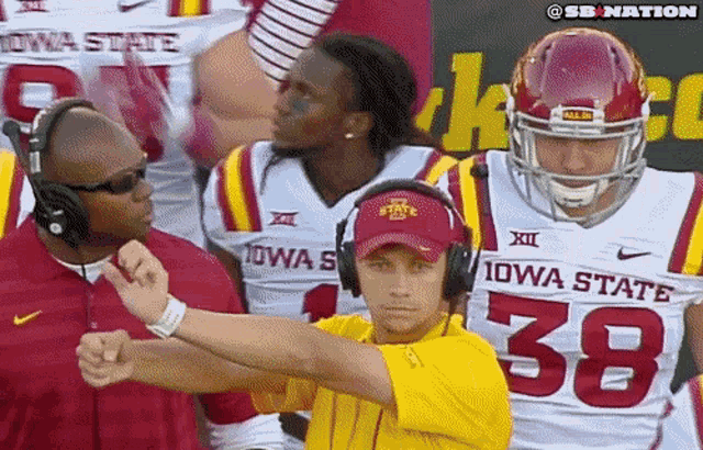 a man wearing a yellow shirt with the number 38 on it stands in front of a group of iowa state football players