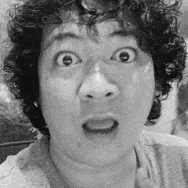 a black and white photo of a man with curly hair making a funny face