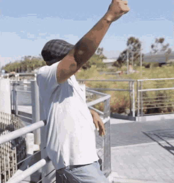 a man wearing a hat and a white shirt is standing on a balcony with his arm in the air