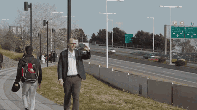 a man in a suit walks down a sidewalk near a highway with a green sign that says ' avenida '