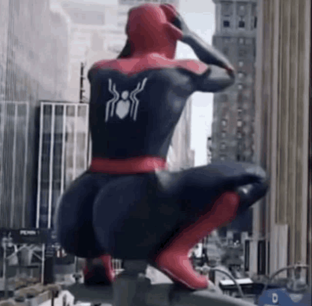 a man in a spiderman costume is squatting on top of a building in a city .