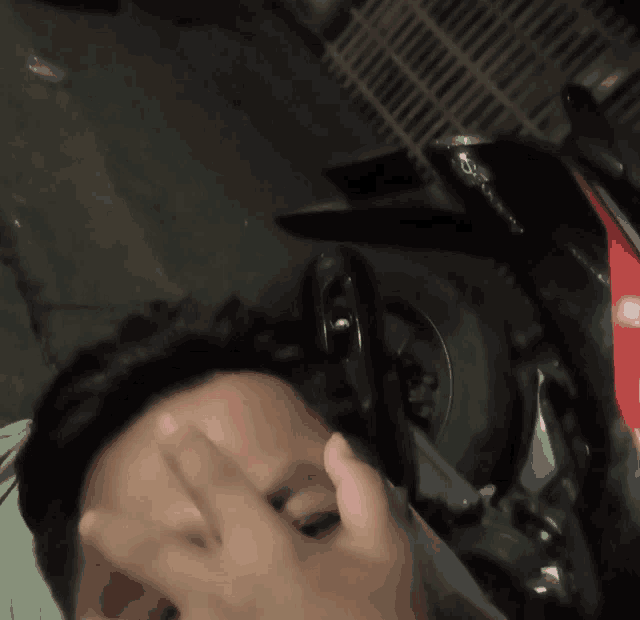 a person covering their face with their hand in front of a red and black motorcycle