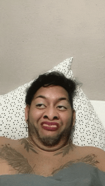 a man with a tattoo on his chest is making a funny face while laying in bed