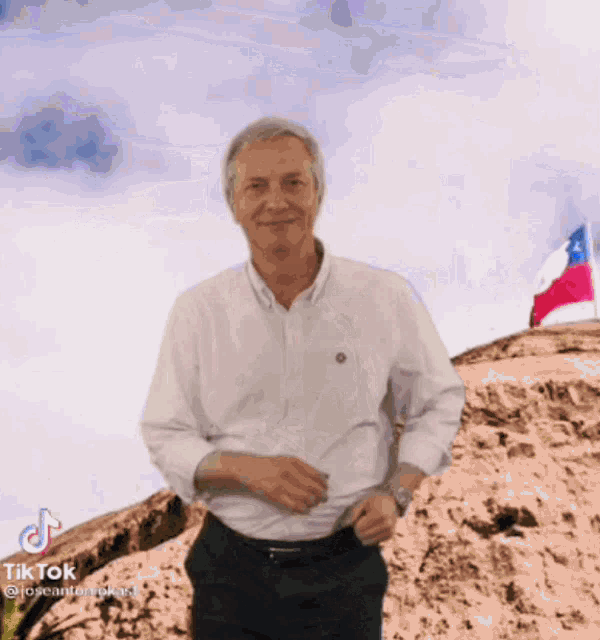 a man in a white shirt is standing in front of a mountain with a flag in the background .