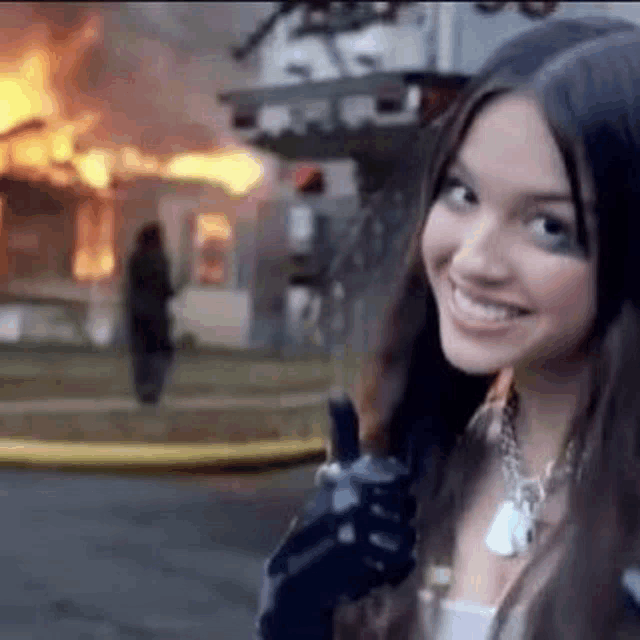 a woman is holding a gun in front of a burning building .