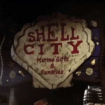 a sign for shell city marine gifts and sundries is hanging on a rope .